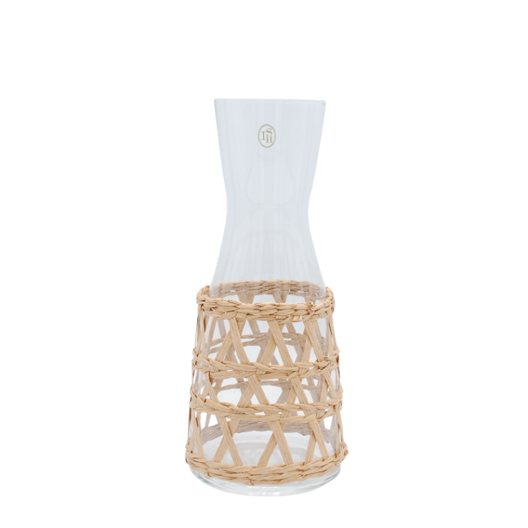 A clear glass carafe with a natural beige woven seagrass wrap around the body.