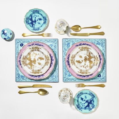 Table setting with decorative plates, bowls, and utensils on a light background