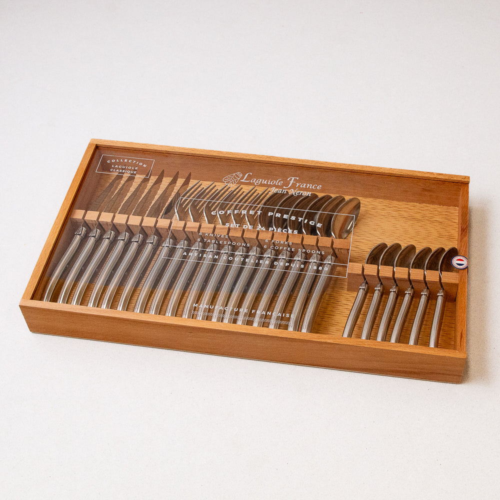 A 24-piece flatware set by Laguiole, consisting of stainless steel utensils, displayed in a wooden storage box with a clear acrylic lid.