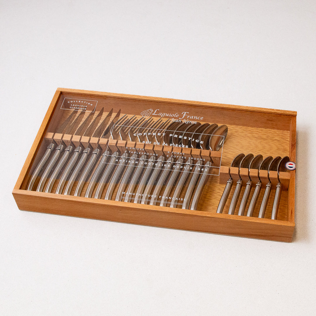 A 24-piece flatware set by Laguiole, consisting of stainless steel utensils, displayed in a wooden storage box with a clear acrylic lid.