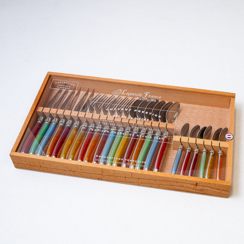 A 24-piece flatware set with rainbow-colored handles displayed in a wooden box with an acrylic lid.