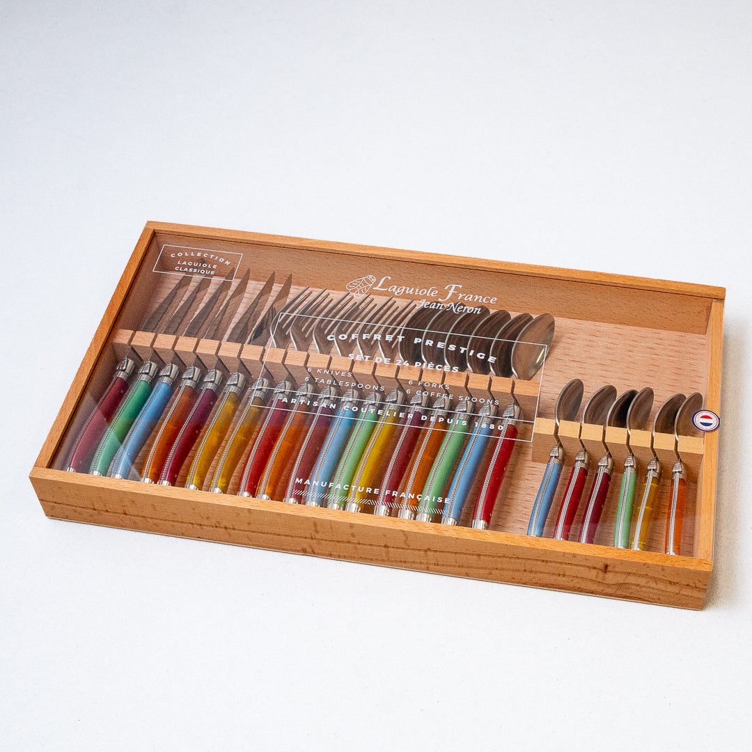 A 24-piece flatware set with rainbow-colored handles displayed in a wooden box with an acrylic lid.