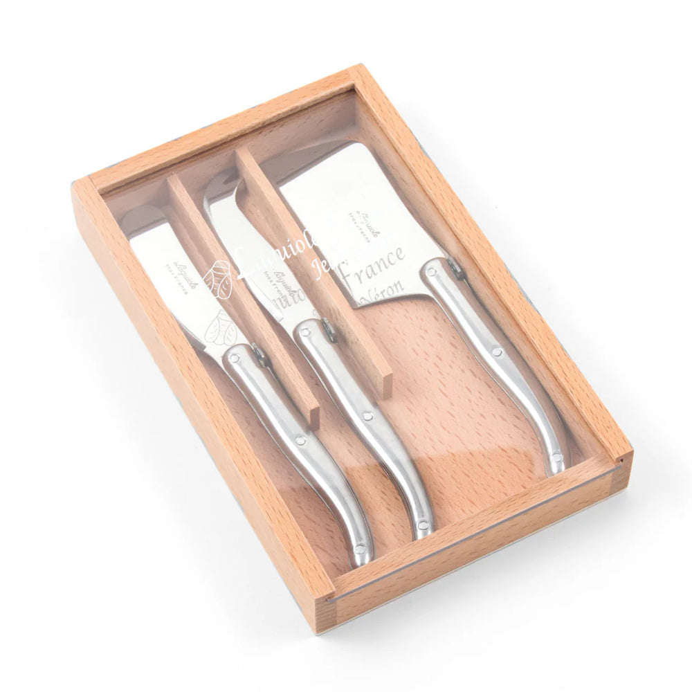 A wooden box with a sliding acrylic lid containing three stainless steel mini cheese tools with wooden handles.