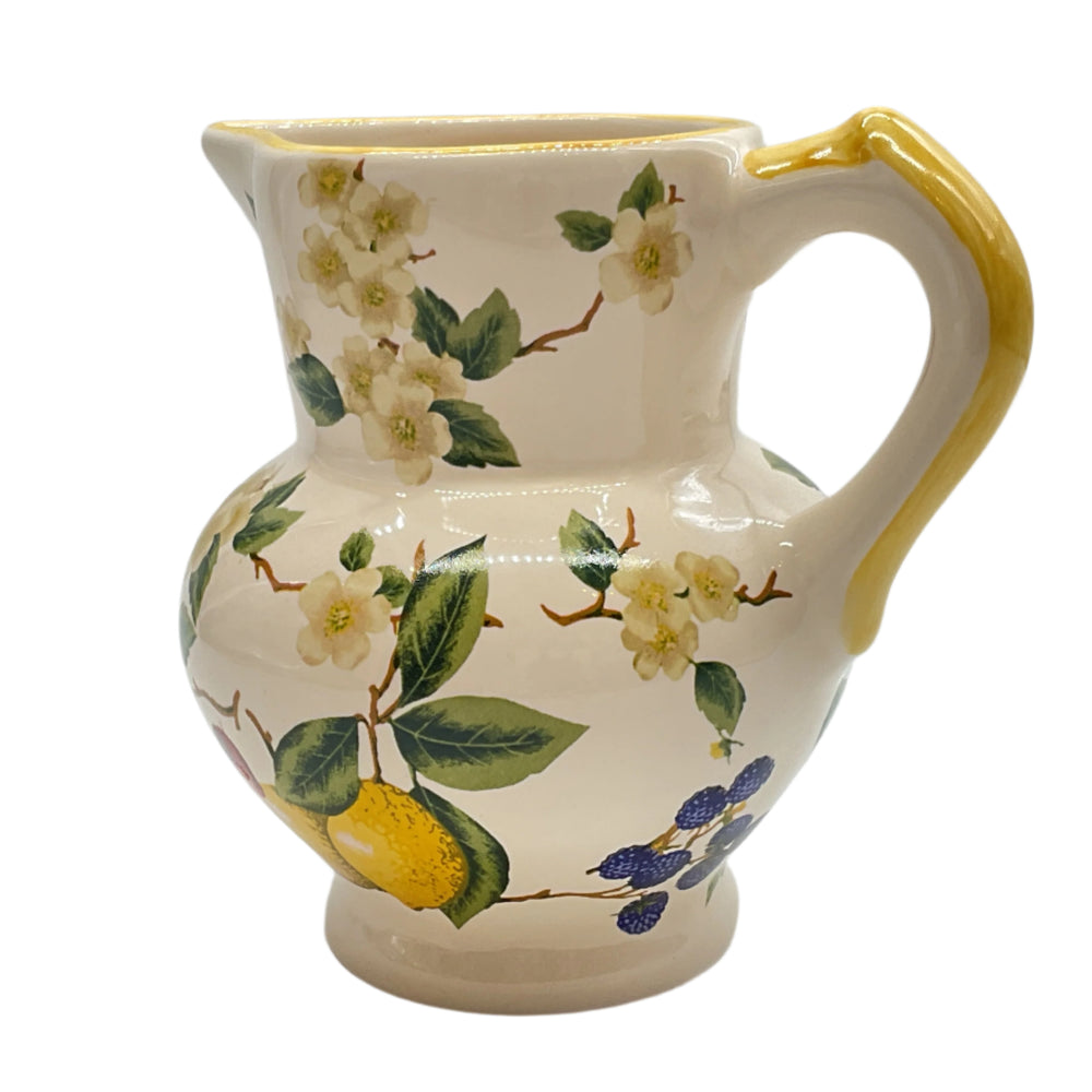 A ceramic pitcher with a floral pattern, featuring lemons and green leaves on a white background, with a yellow handle.