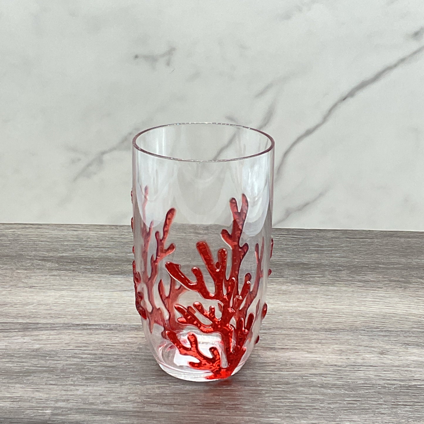 A clear acrylic highball glass with a red coral reef design on the exterior.