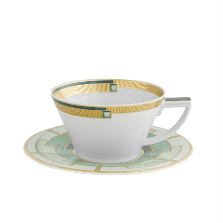A white ceramic tea cup with green and gold geometric patterns on the saucer and cup.